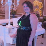 Young woman in black dress by white grand piano