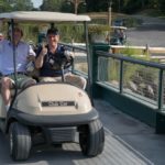 Two men in a golf cart driving over a bridge give the camera a thumbs up at the 2013 Howard F. Treiber Memorial Golf Outing