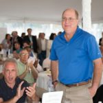 Man standing with his hands in his pockets while attendees around him applaud at the 2013 Howard F. Treiber Memorial Golf Outing